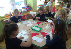 Dzieci przy stolikach przyklejają paseczki do talerzyków.